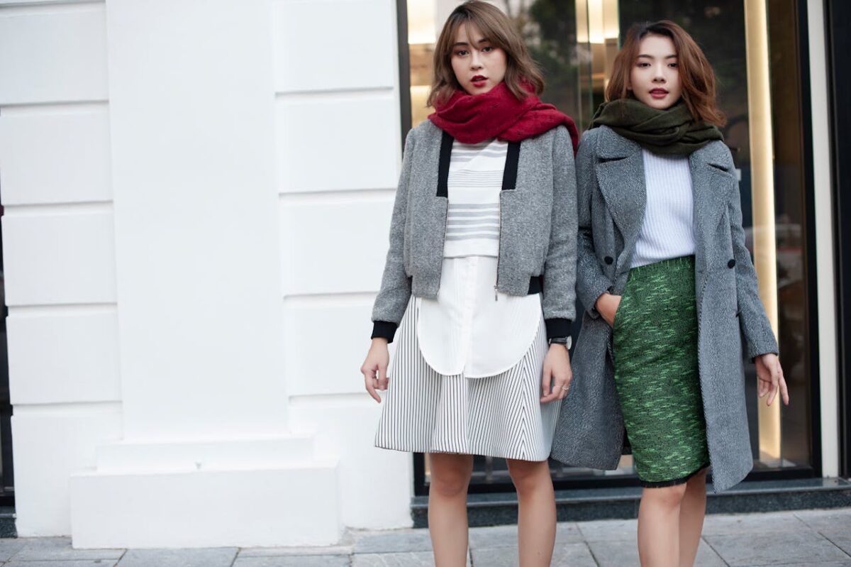 about-02 Two women wearing stylish winter coats and scarves posing confidently outdoors.